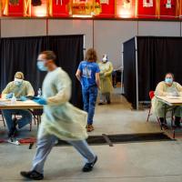 Person waits for a COVID test while people wearing medical gear hurry by