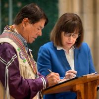 Two people sign a document on a podium