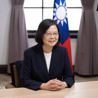 Person wearing business clothes sits at a desk, smiling