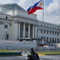 Motorcycle drives past a stone "National Museum" fronted by the Philippine flag