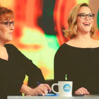 Two people appearing on a TV talk show, sitting at a desk with mugs in front of them