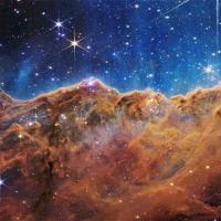 A field of stars in the background and in the foreground a colorful cliff-shaped mass of cosmic gases.