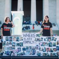 Two young people standing behind a large sign filled with snapshots of people