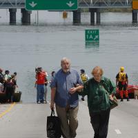  An older man and woman carrying luggage walk away from boats pulled to the edge of a flooded highway in New Orleans