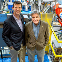 Two physicsists stand in front of accelerator equipment