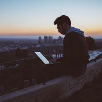 Person looking at a laptop while sitting on a rooftop at sunset