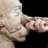 Hand grasping clay nose of bust of a man