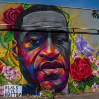 Artist drawing of George Floyd&#039;s face on a wall, surrounded by flowers and Black Lives Matter sign