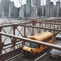 Yellow bus on a bridge, New York City in the background