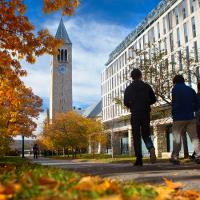 Two people walk past a building; fall leaves