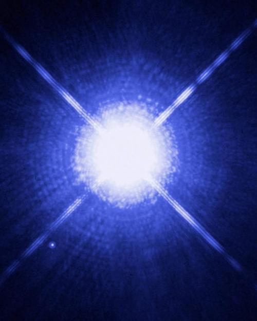 Four lines of light radiating out from a white dwarf star on a blue background.