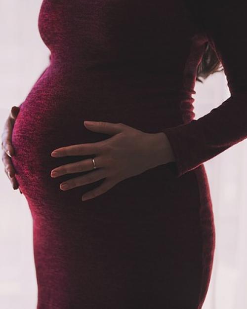 Pregnant woman in tight red dress with hands on stomach.