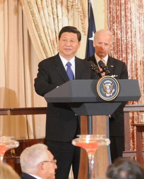 Chinese President Xi Jinping standing at a podium with the US Seal on the front, with Joe Biden behind him and Hilary Clinton to his left dressed in a red pants suit.