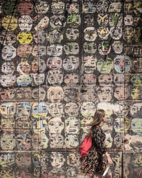 Person walking past a wall painted with many faces