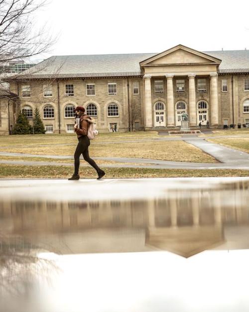 		person walks past a puddle that is reflecting a campus building
	