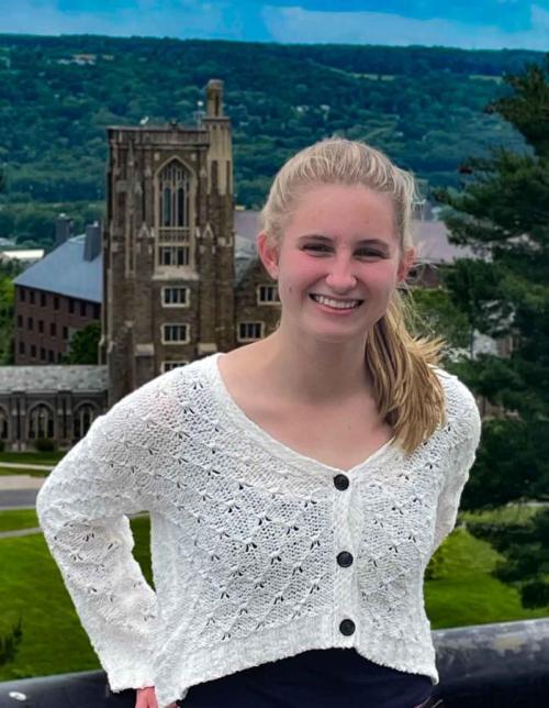 Catherine Cherry in a white sweater, smiling, with Cornell's Libe Slope in the background.