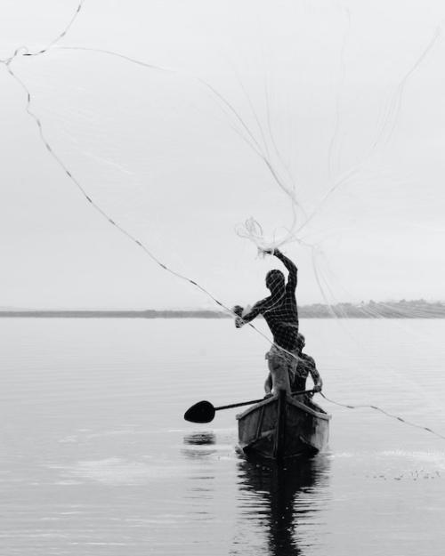 Person casts a net from a canoe on a calm lake