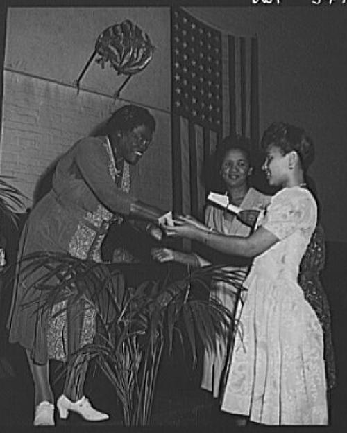 		Black and white historic photo of one person giving an award to another on a stage
	