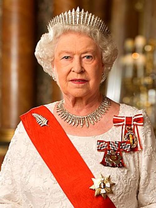 Wearing a tiara with matching shiney necklace, a sash and medals, the white haired queen looks unsmilingly at the camera.