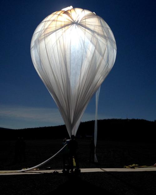 Light shines through gossamer fabric of a large, inflated balloon against a dark sky