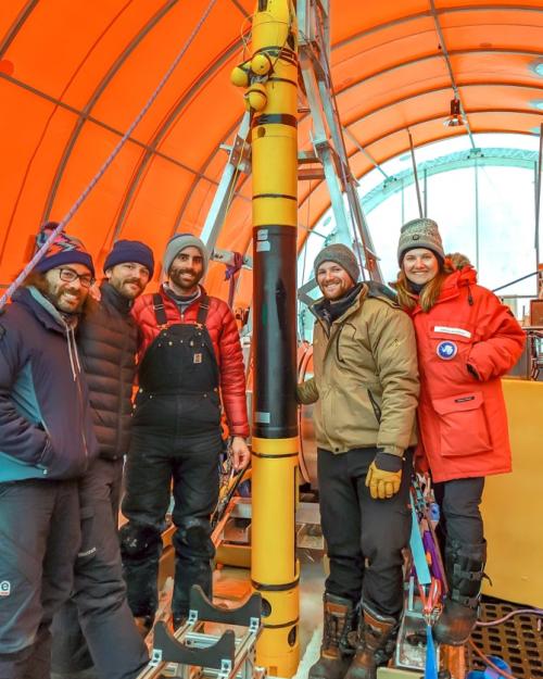 		Four people in winter gear stand around a tall, thin piece of equipment
	