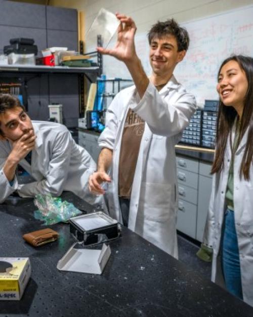 four people in lab coats look at a small, rectangular object together