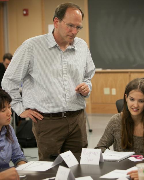Steven Strogatz standing next to a table of students who are working on a math problem