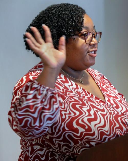 Person speaks at a podium, gesturing with one hand