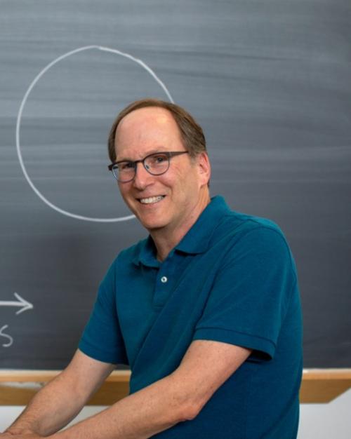 Steven Strogatz in front of a blackboard with "small world" and an illustration on it showing a circle and interconnected lines inside