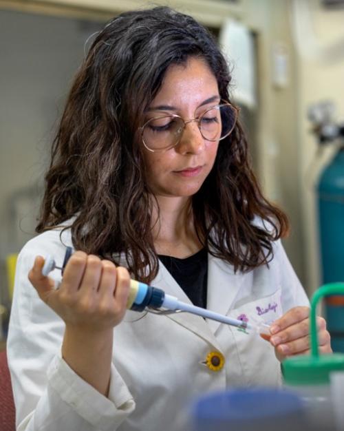 		Person in a white lab coat piping something into a test tube
	