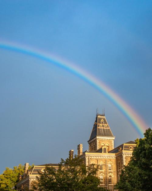 		A rainbow against a deep blue sky, over a brick building with a peaked roof
	