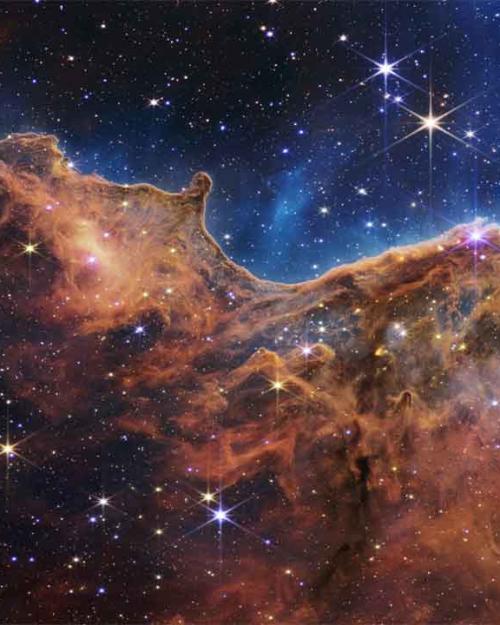 		A field of stars in the background and in the foreground a colorful cliff-shaped mass of cosmic gases.
	