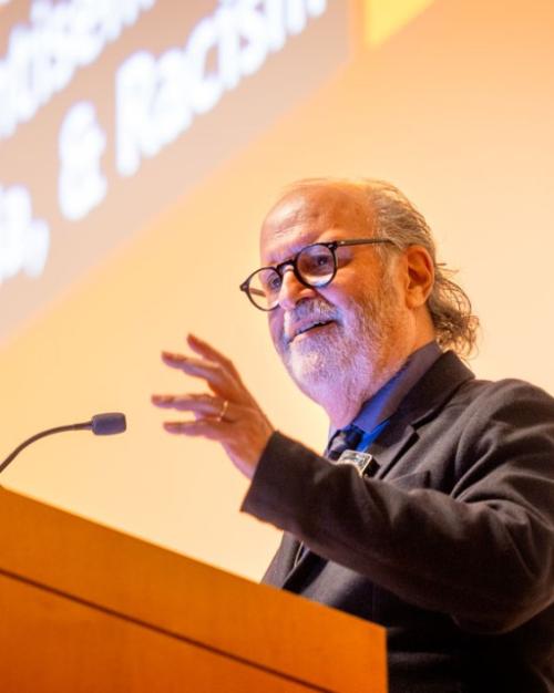 Person gestures from behind a podium with a microphone