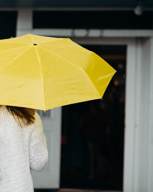 Bright yellow umbrella held by a person wearing a white sweater. It's not raining. 