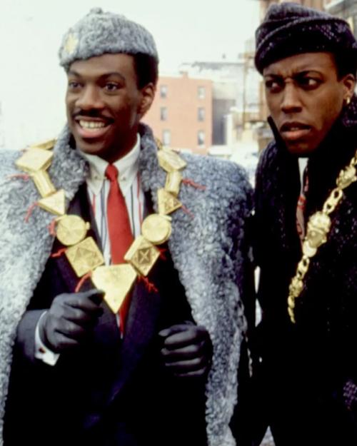 		Two people -- characters in a film -- wearing large coats and gold jewelry
	