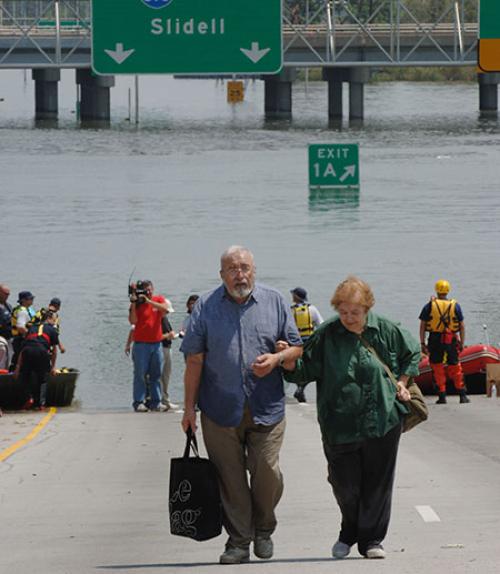  An older man and woman carrying luggage walk away from boats pulled to the edge of a flooded highway in New Orleans