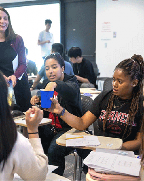 Five students in a circle with a teacher looking on