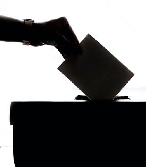 Silhouette of a hand putting a ballot on a box