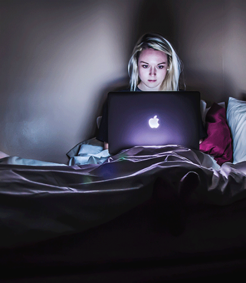 Woman in dark room gazing into computer screen