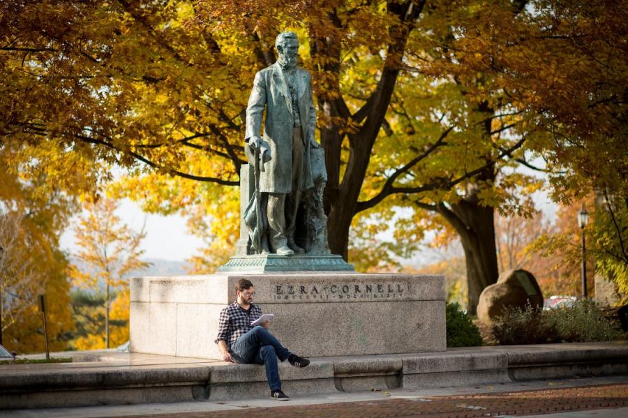 Student reading a book by statue of Ezra Cornell