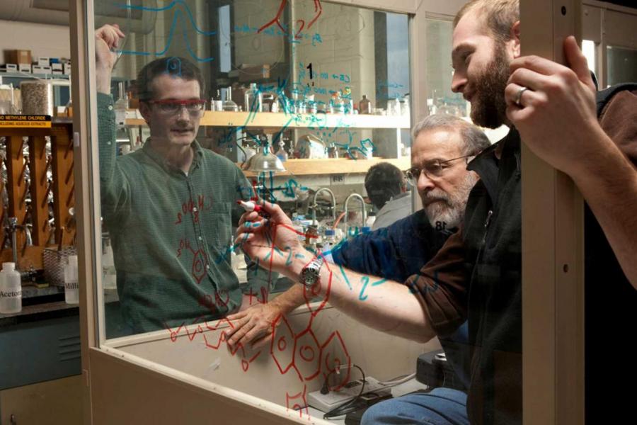 professor and two student write formulas on clear glass