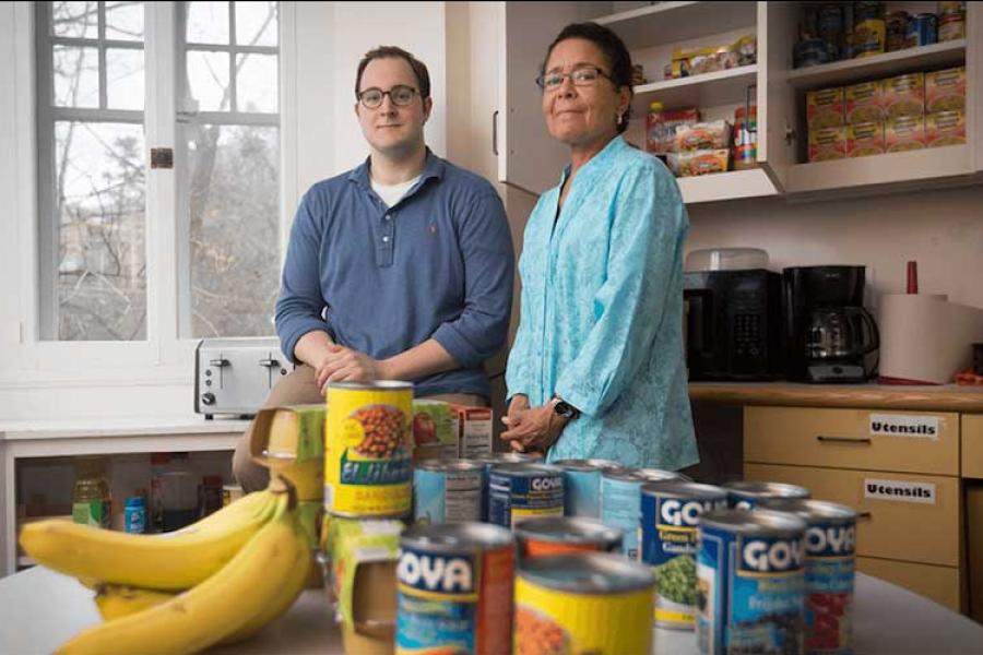 Two people standing behind a stack of groceries: canned beans and bananas