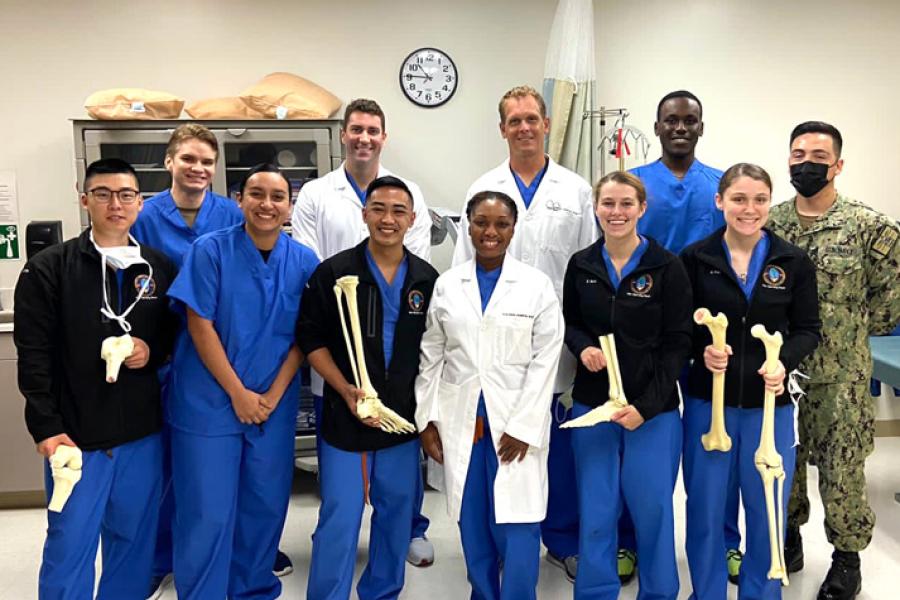 Eleven people in medical scrubs - a surgical team - poses for a picture. Some hold model leg bones