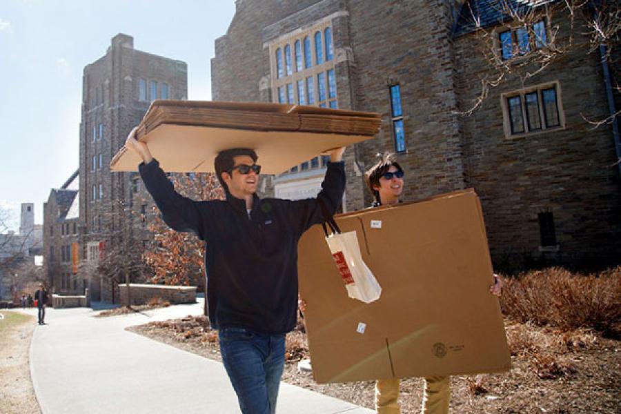 Two students carrying boxes across campus