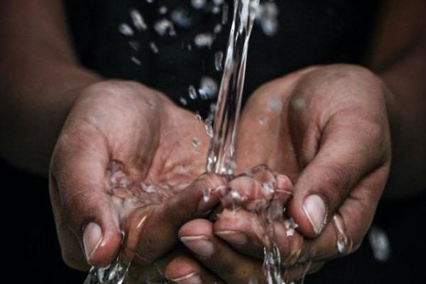 Dark-skinned person cupping hands under a stream of water. 