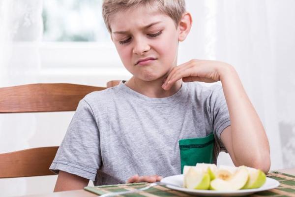 Child making a face at a cut up apple on a plate