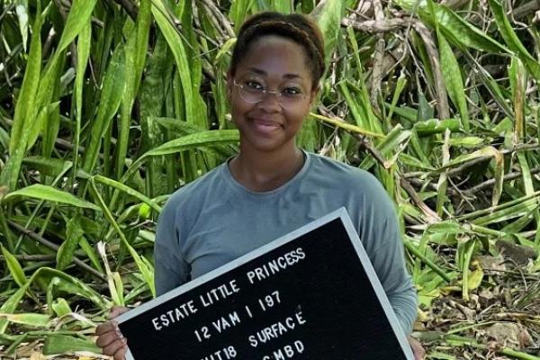 Person standing in a field holding a sign that says "Estate Little Princess"