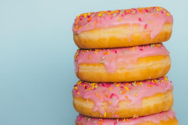 Four donuts in a stack: frosted pink, covered with sprinkles