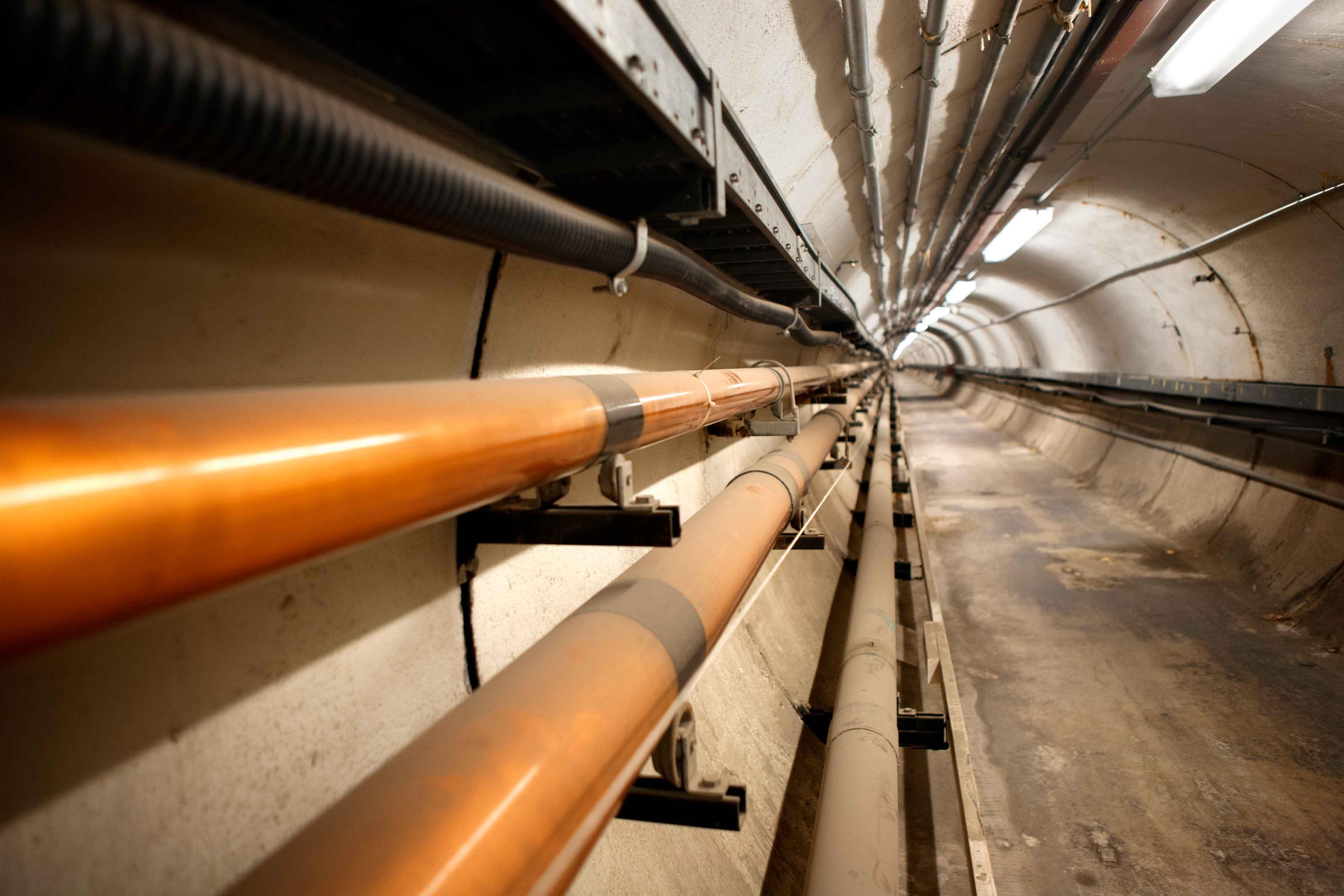 A long cement tunnel with pipes and cables running along it.
