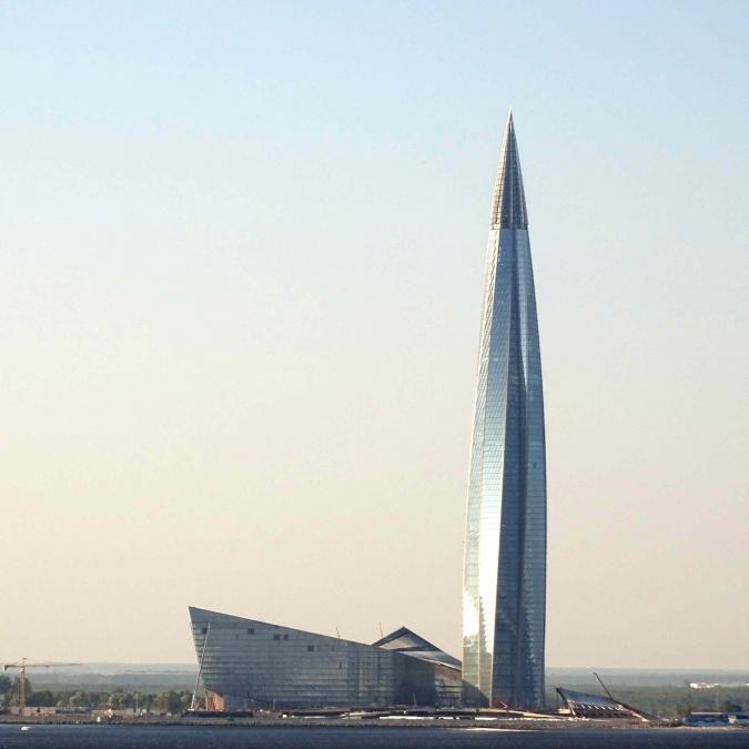 A rocketship-shaped skyscraper next to a building shaped like the prow of a ship, both steel-colored.